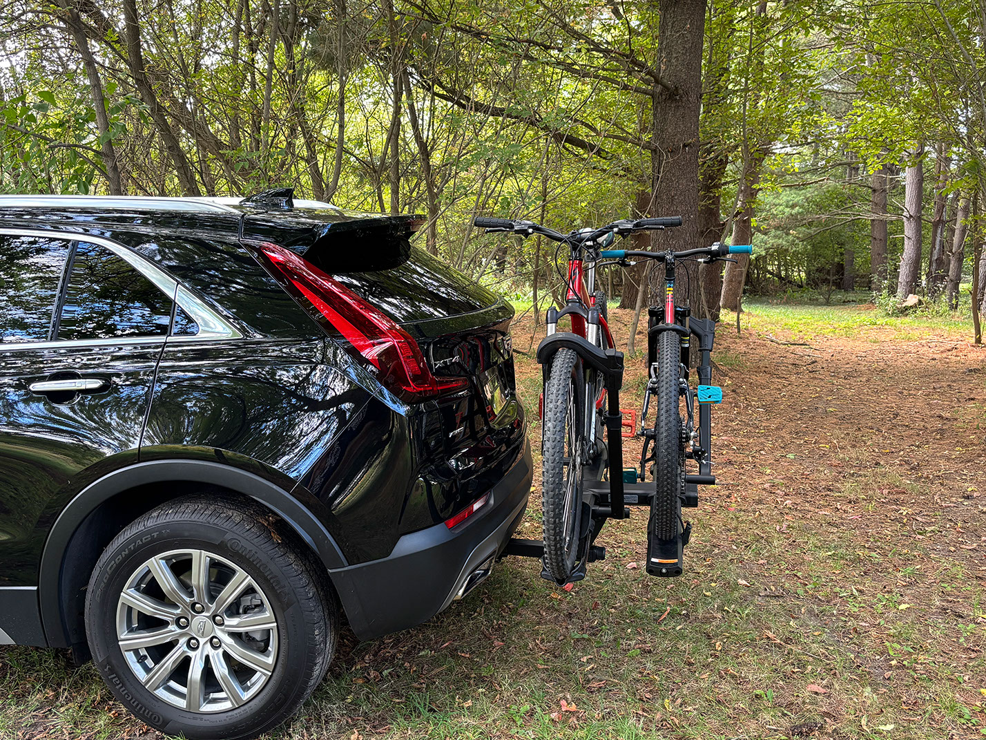 Black Volvo XC40 with hitch-mounted bike rack carrying two mountain bikes in a forest setting.