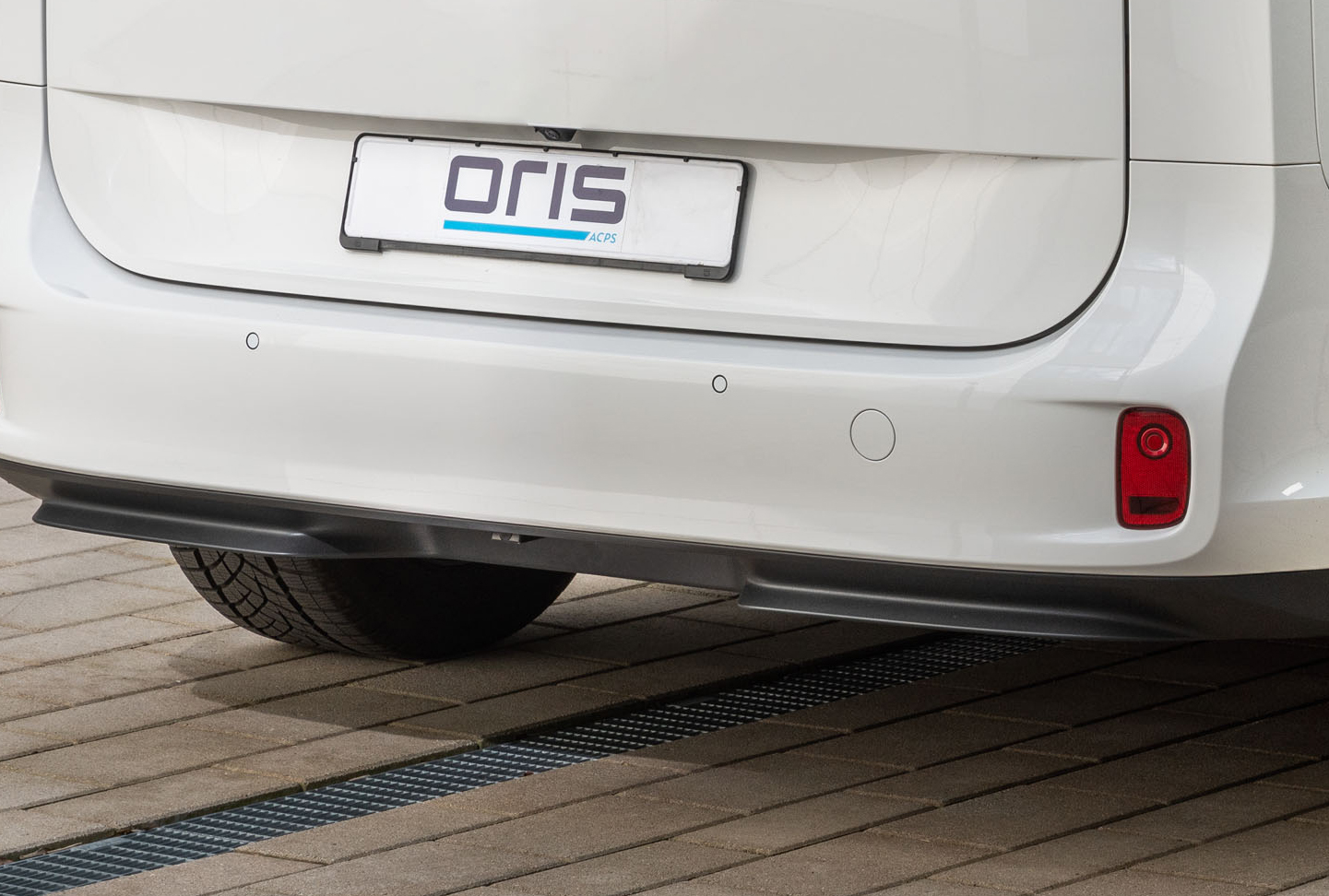 Rear view of a white vehicle with hidden ORIS retractable receiver hitch fully stowed behind the rear bumper on a paved surface.