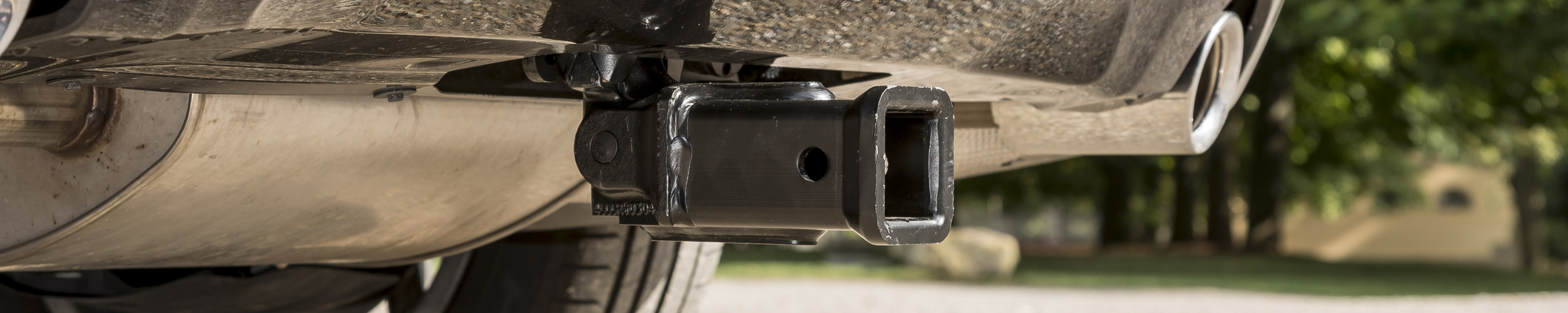 Close-up of a detachable US trailer hitch receiver mounted beneath a vehicle with a green landscape in the background.
