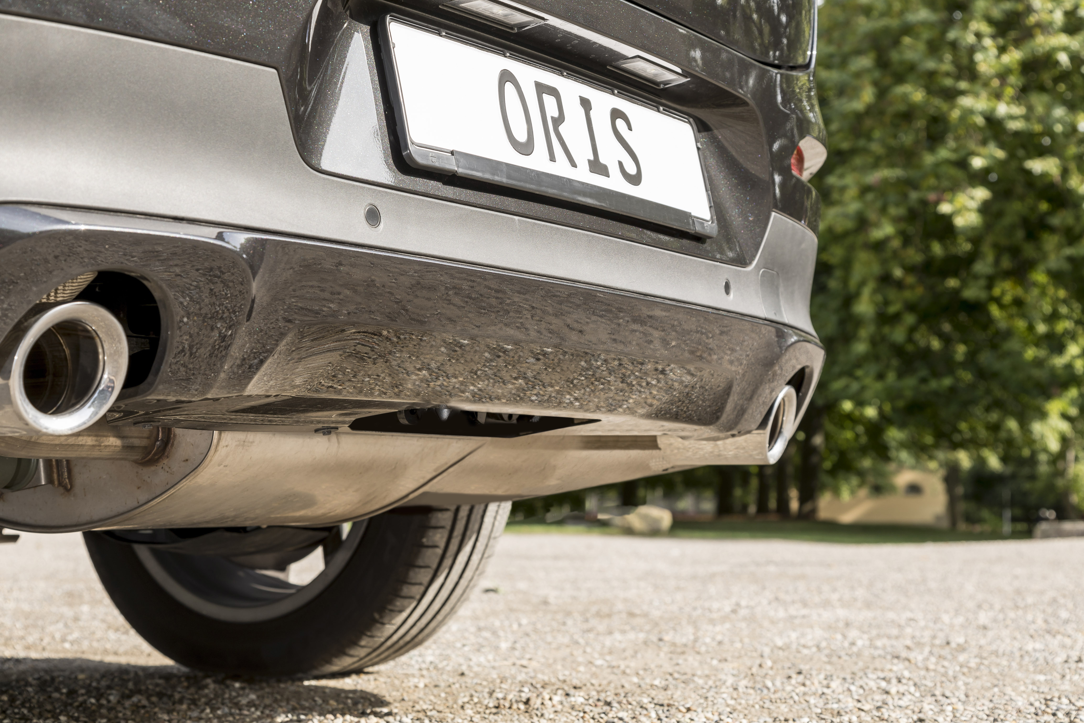 Rear view of a dark grey vehicle with hidden ORIS detachable receiver hitch removed from the mounting point beneath the rear bumper on a gravel surface.
